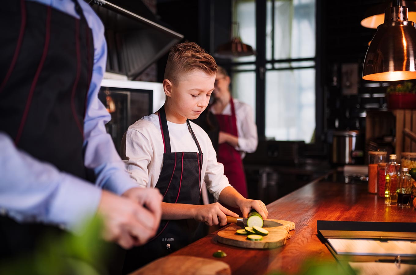 le tablier | Junge in Küche beim Schneiden von Gemüse mit schwarzer Schürze