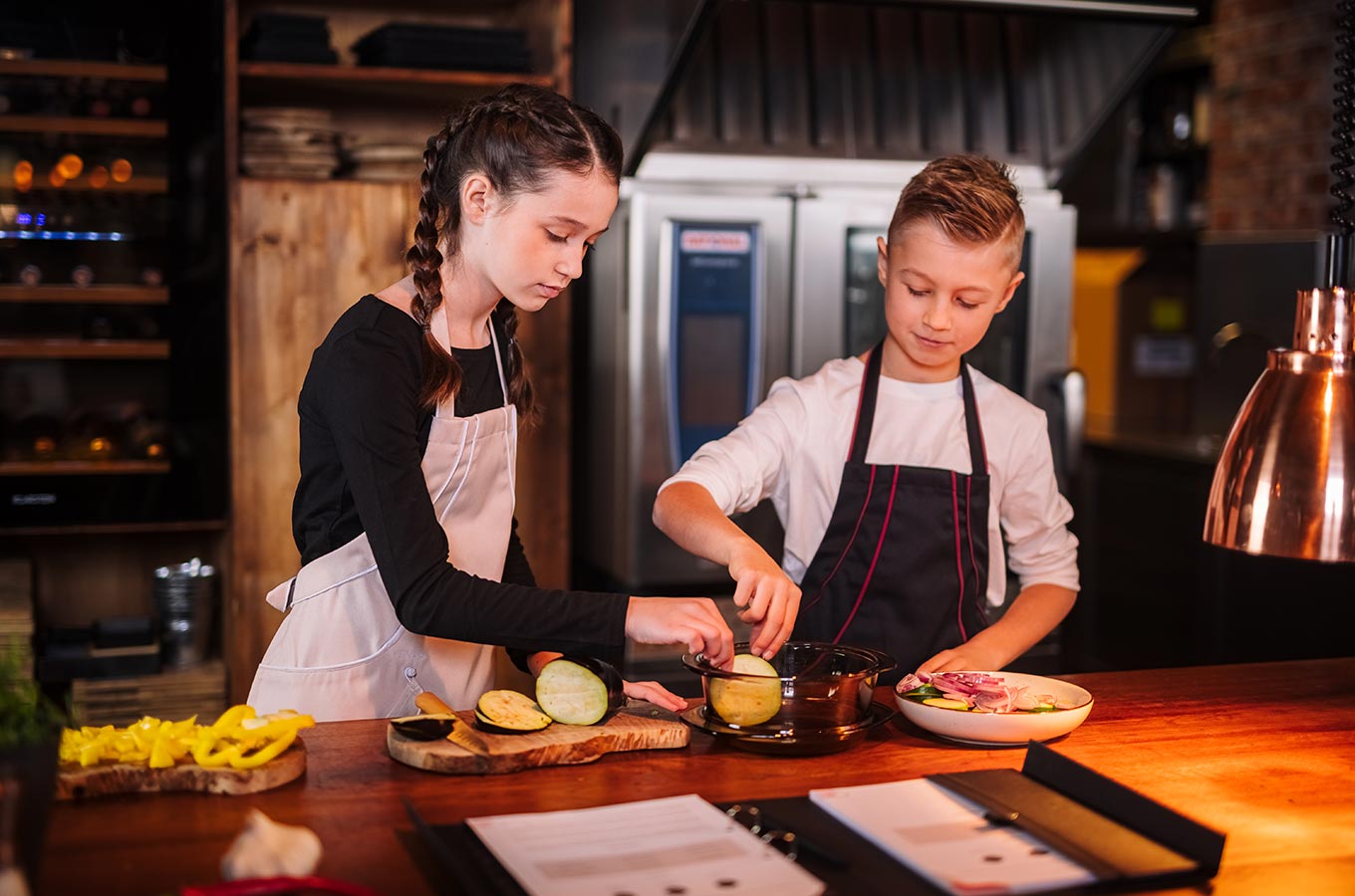 le tablier | Mädchen und Junge in der Küche beim Kochen mit rosa und schwarzer Schürze
